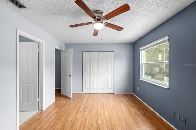 unfurnished bedroom with ceiling fan, a textured ceiling, light wood-type flooring, and a closet