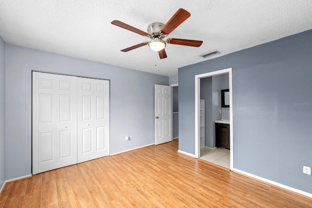 unfurnished bedroom with ceiling fan, a textured ceiling, light hardwood / wood-style floors, and a closet