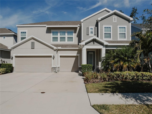 craftsman house featuring roof with shingles, stucco siding, an attached garage, stone siding, and driveway