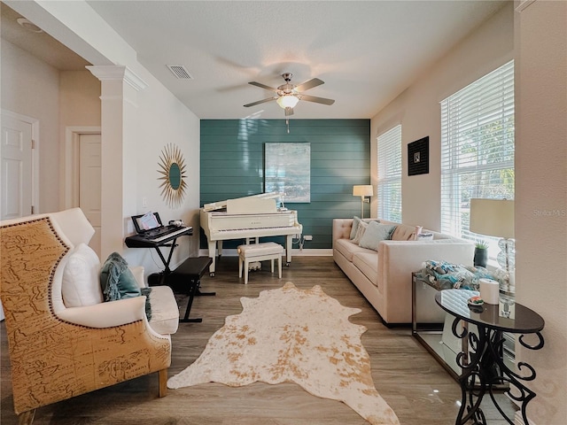 living area with decorative columns, visible vents, ceiling fan, wood finished floors, and wood walls