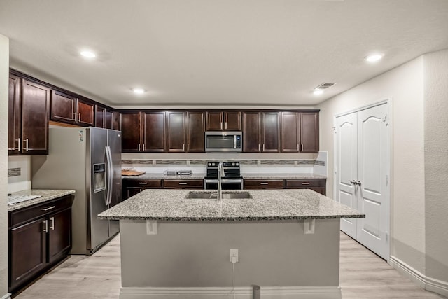 kitchen with sink, a kitchen breakfast bar, a kitchen island with sink, stainless steel appliances, and light stone countertops