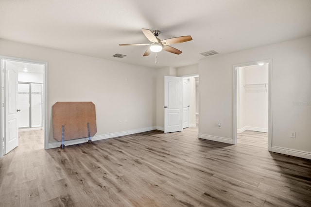 unfurnished bedroom featuring a walk in closet, light hardwood / wood-style flooring, a closet, and ceiling fan