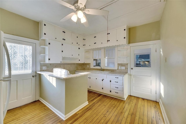 kitchen with sink, tile countertops, light wood-type flooring, kitchen peninsula, and white cabinets