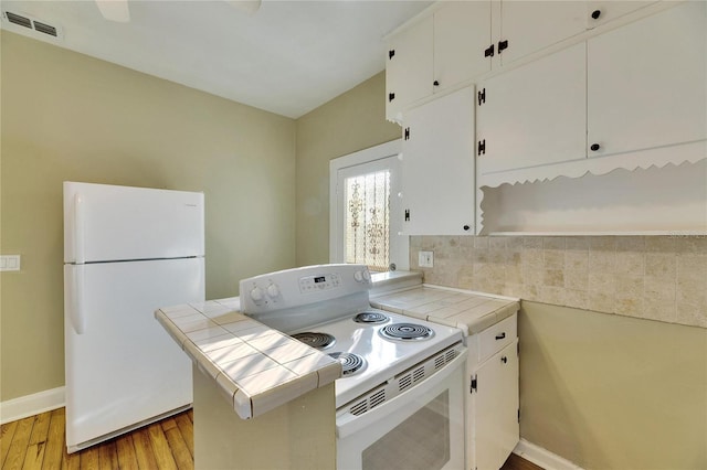 kitchen with light hardwood / wood-style flooring, tile counters, kitchen peninsula, white appliances, and white cabinets