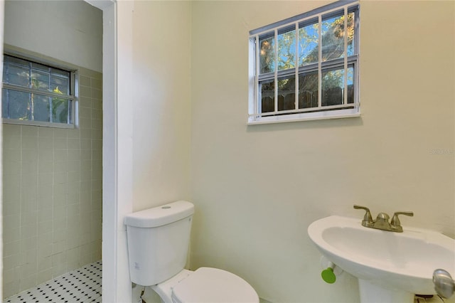 bathroom featuring tiled shower, toilet, and sink