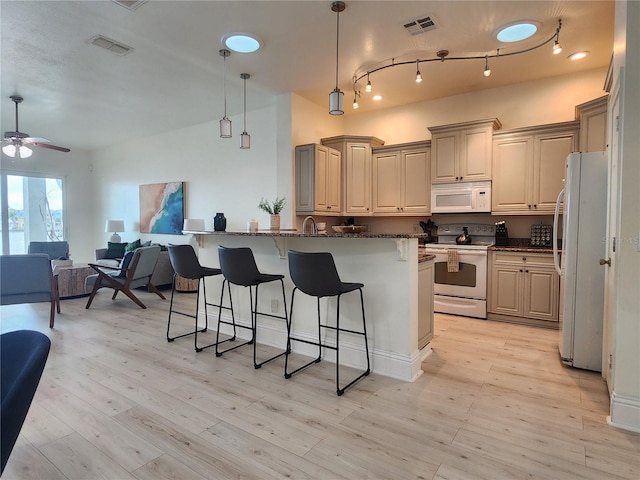 kitchen featuring pendant lighting, a breakfast bar area, dark stone counters, white appliances, and light wood-type flooring