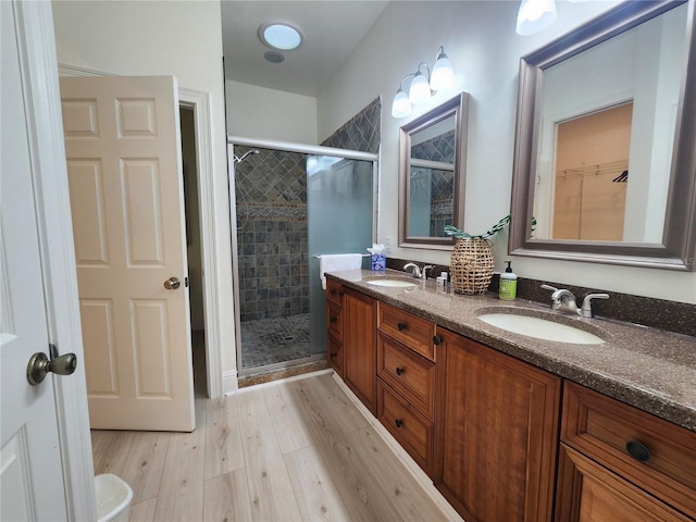 full bathroom featuring double vanity, a stall shower, a sink, and wood finished floors