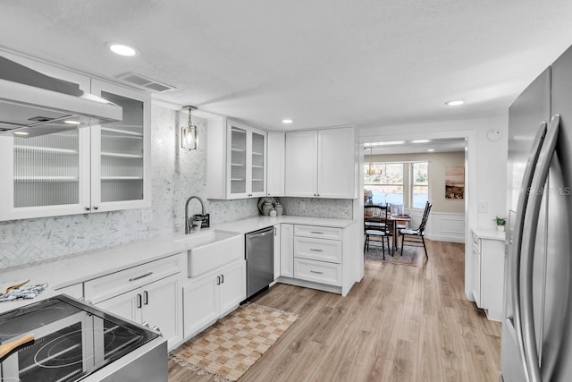 kitchen featuring pendant lighting, sink, white cabinets, stainless steel appliances, and light hardwood / wood-style flooring