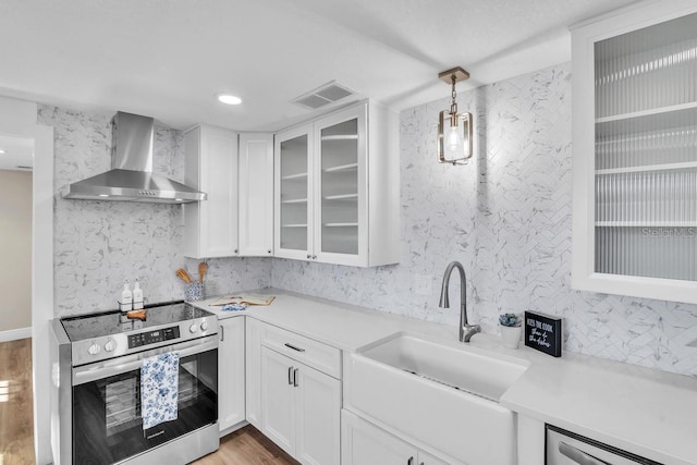 kitchen featuring wall chimney exhaust hood, hanging light fixtures, stainless steel electric stove, light hardwood / wood-style floors, and white cabinets