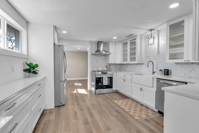 kitchen with decorative light fixtures, sink, white cabinets, stainless steel appliances, and wall chimney range hood