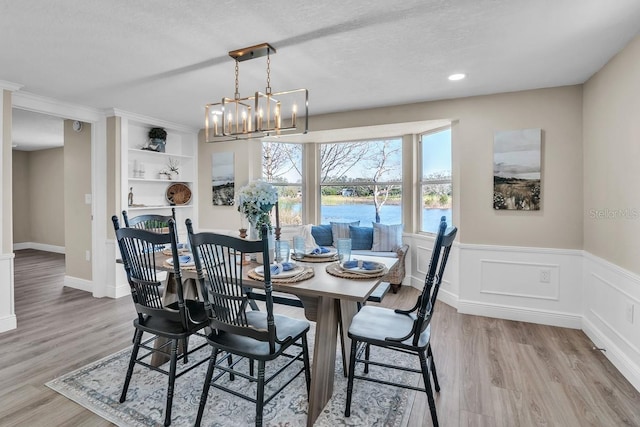 dining area with a water view, an inviting chandelier, light hardwood / wood-style flooring, and a textured ceiling