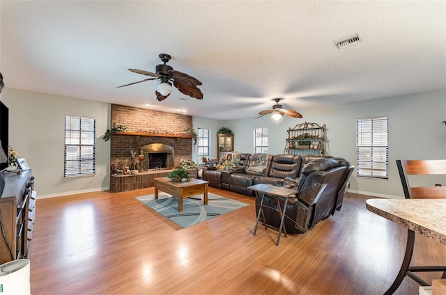 living room featuring hardwood / wood-style flooring, a brick fireplace, a healthy amount of sunlight, and a textured ceiling