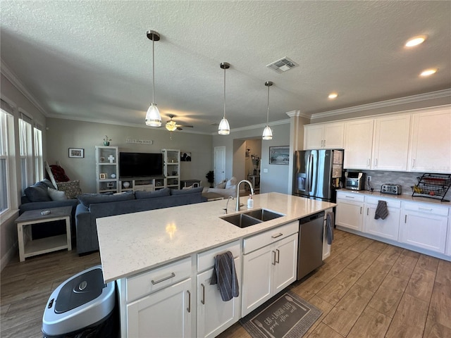 kitchen featuring appliances with stainless steel finishes, decorative light fixtures, white cabinetry, sink, and a center island with sink