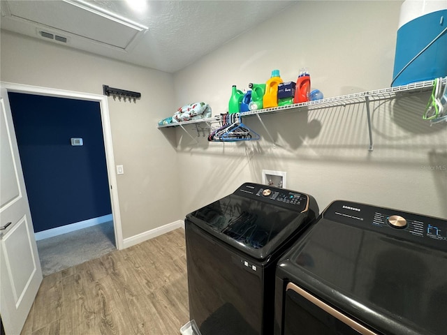 clothes washing area with wood-type flooring, washing machine and clothes dryer, and a textured ceiling