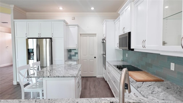 kitchen with appliances with stainless steel finishes, white cabinetry, a kitchen bar, crown molding, and light stone countertops