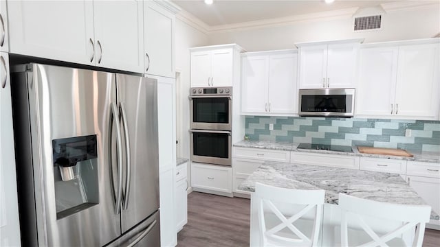 kitchen featuring appliances with stainless steel finishes, backsplash, a kitchen breakfast bar, light stone countertops, and white cabinets