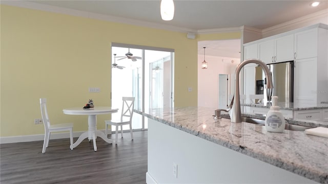 kitchen featuring pendant lighting, white cabinets, crown molding, light stone countertops, and dark wood-type flooring