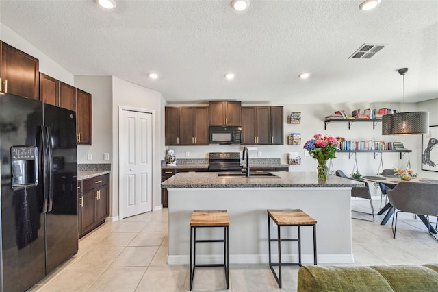 kitchen with light tile patterned flooring, a breakfast bar, sink, a center island with sink, and black appliances