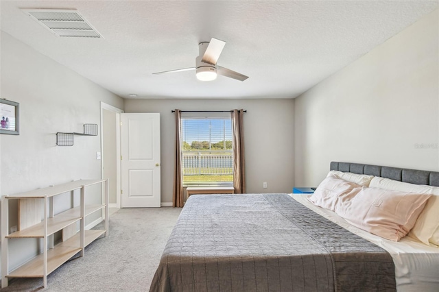 bedroom featuring a textured ceiling, light colored carpet, and ceiling fan