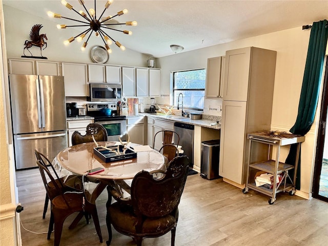 kitchen with sink, light stone counters, appliances with stainless steel finishes, a notable chandelier, and light hardwood / wood-style floors