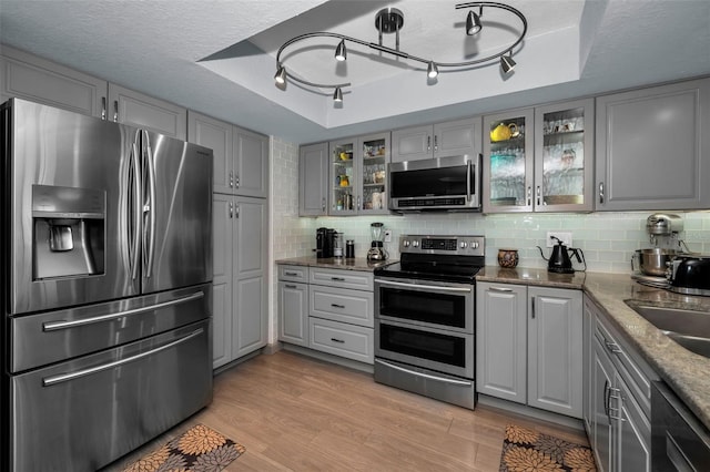 kitchen with appliances with stainless steel finishes, a tray ceiling, gray cabinets, and light wood-type flooring