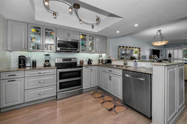 kitchen featuring sink, gray cabinets, stainless steel appliances, a raised ceiling, and kitchen peninsula