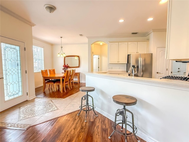 kitchen featuring pendant lighting, white cabinetry, ornamental molding, stainless steel appliances, and light hardwood / wood-style flooring