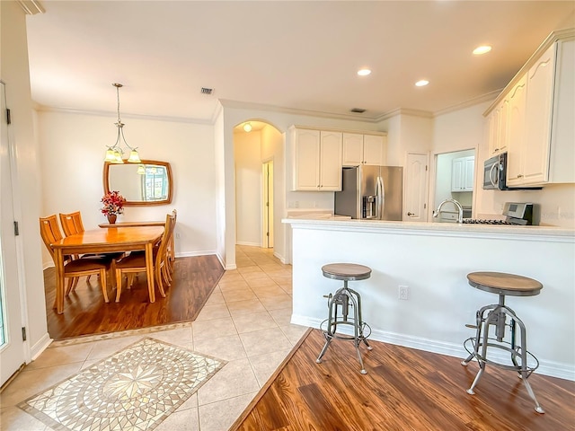 kitchen with appliances with stainless steel finishes, white cabinetry, hanging light fixtures, light tile patterned floors, and kitchen peninsula