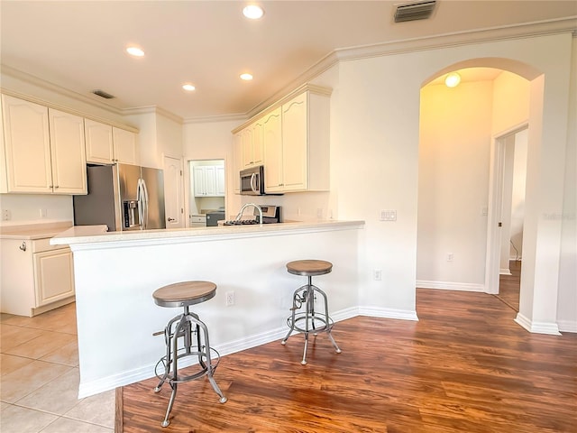 kitchen with white cabinetry, a kitchen bar, kitchen peninsula, stainless steel appliances, and crown molding