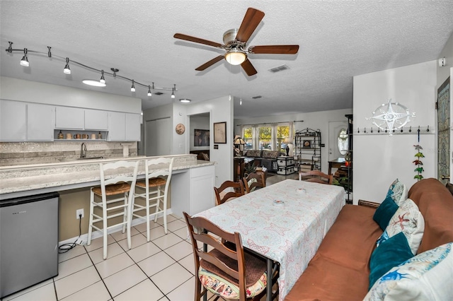 dining space featuring ceiling fan, sink, light tile patterned floors, and a textured ceiling