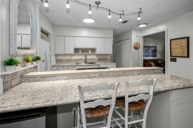 kitchen featuring a kitchen bar, sink, white cabinetry, dishwasher, and backsplash