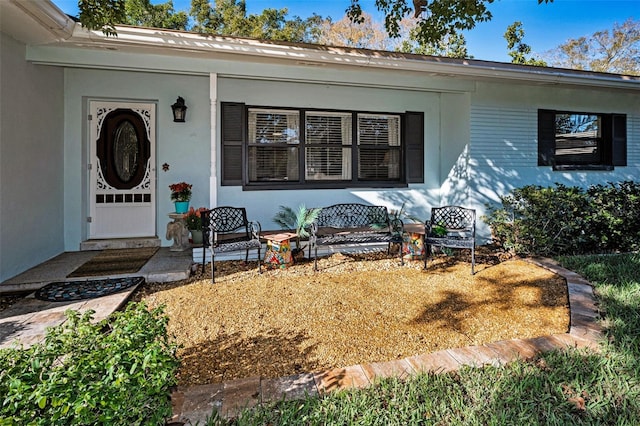 doorway to property featuring covered porch and stucco siding