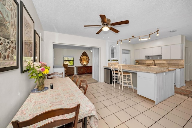 kitchen with a breakfast bar area, light tile patterned floors, light countertops, white cabinets, and a sink