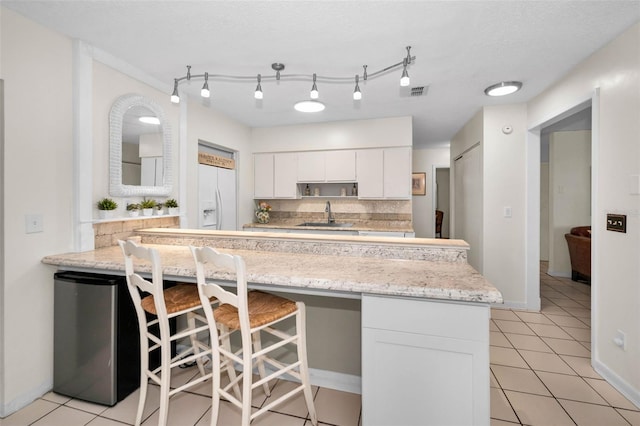 kitchen with light tile patterned floors, a breakfast bar, white fridge with ice dispenser, white cabinetry, and a sink