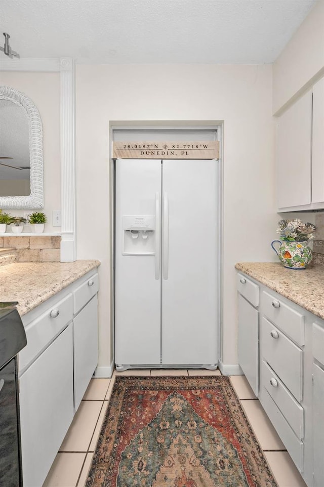 kitchen featuring light tile patterned floors, white refrigerator with ice dispenser, and white cabinets