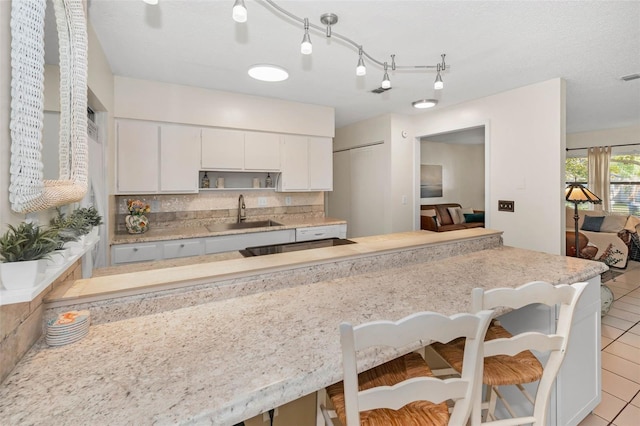 kitchen featuring light tile patterned floors, a breakfast bar area, a sink, white cabinetry, and decorative backsplash