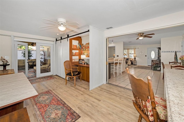 interior space featuring a barn door, visible vents, ceiling fan, light wood-style flooring, and french doors