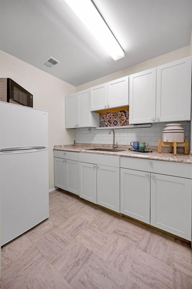 kitchen featuring black microwave, a sink, visible vents, backsplash, and freestanding refrigerator