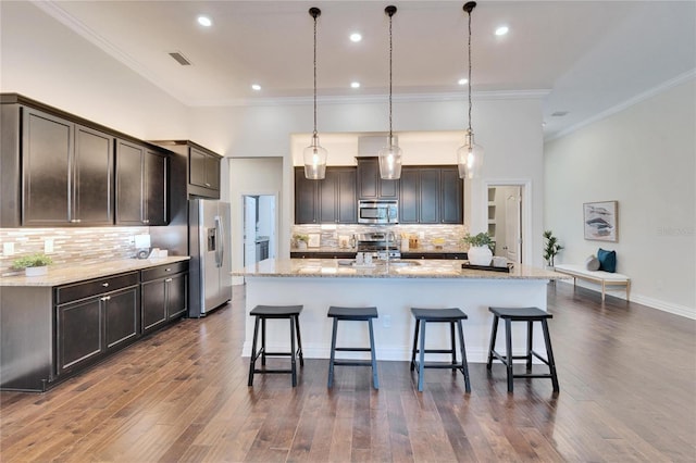 kitchen with pendant lighting, backsplash, stainless steel appliances, a spacious island, and dark brown cabinetry