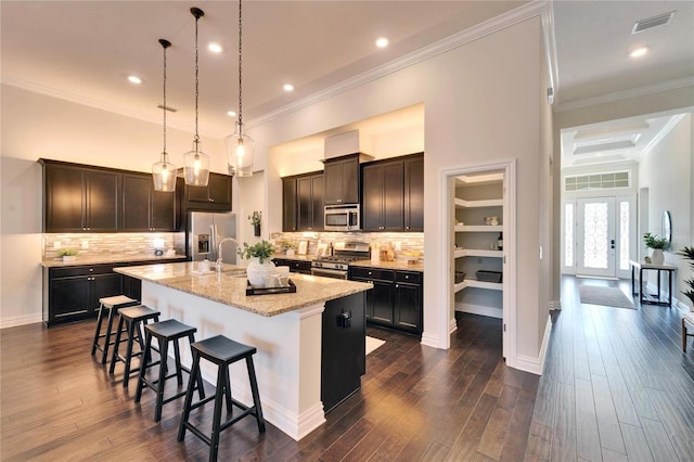 kitchen with a kitchen breakfast bar, ornamental molding, a kitchen island with sink, light stone counters, and stainless steel appliances