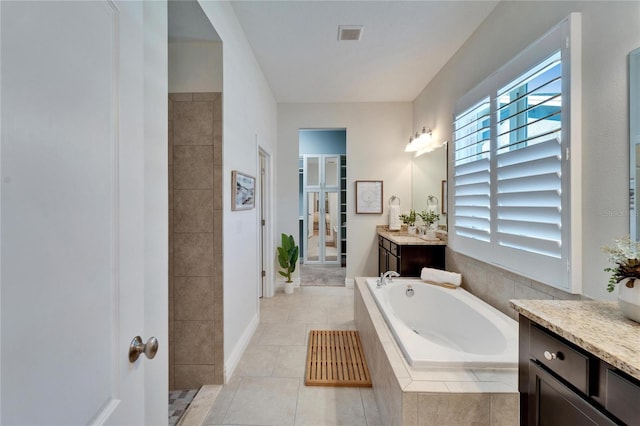 bathroom featuring a relaxing tiled tub, vanity, and tile patterned flooring