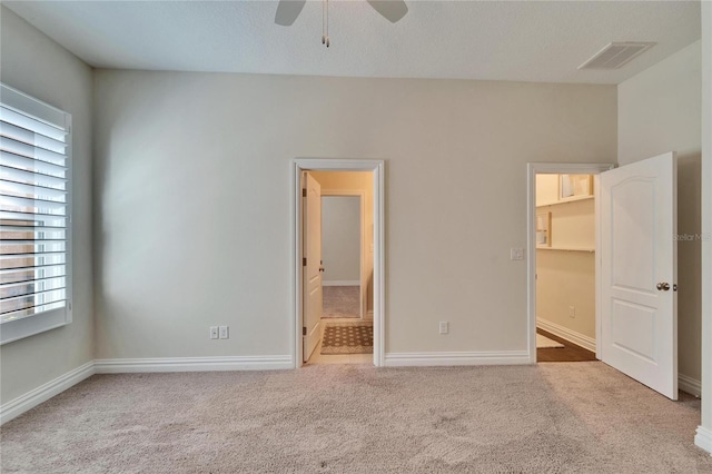 unfurnished bedroom featuring a spacious closet, light colored carpet, ceiling fan, and ensuite bathroom