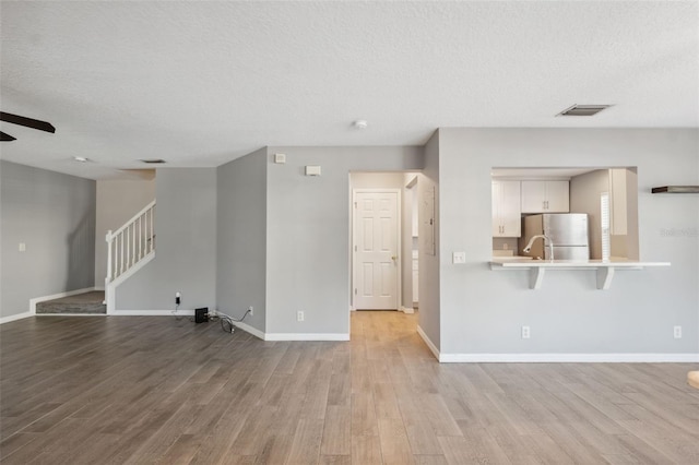 unfurnished living room with ceiling fan, a textured ceiling, and light hardwood / wood-style floors