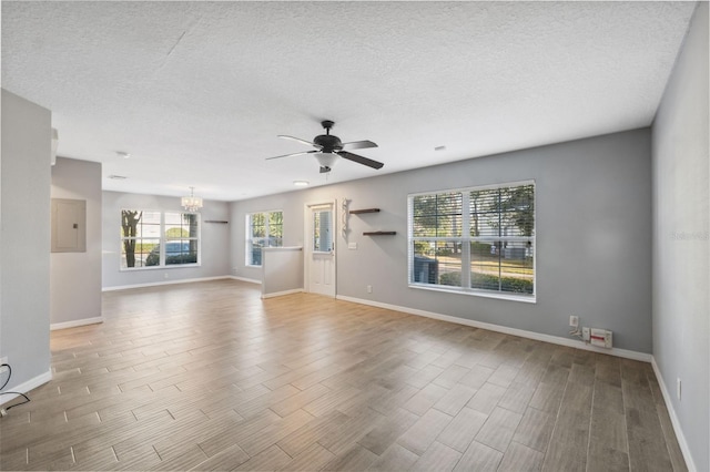 empty room featuring plenty of natural light, electric panel, ceiling fan with notable chandelier, and a textured ceiling