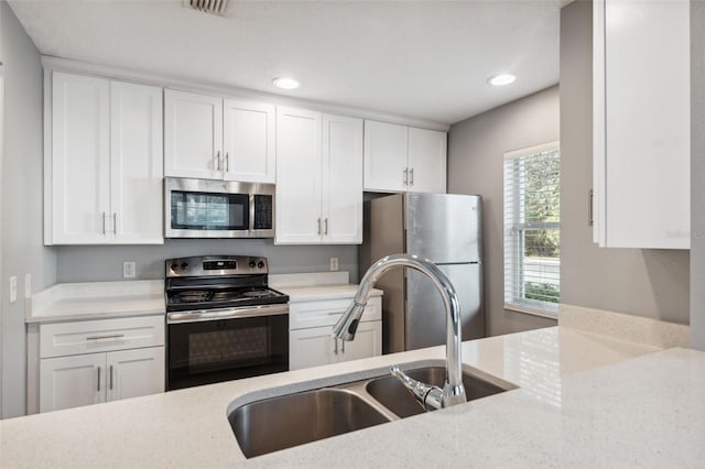 kitchen featuring white cabinetry, sink, light stone counters, and appliances with stainless steel finishes