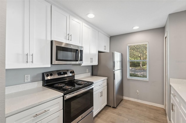 kitchen with light stone countertops, white cabinetry, appliances with stainless steel finishes, and light wood-type flooring