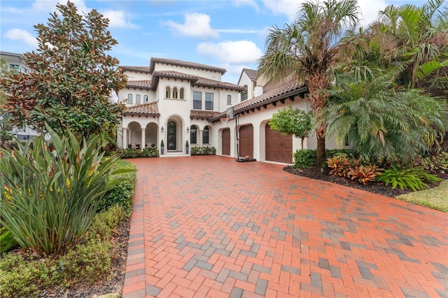 mediterranean / spanish house featuring decorative driveway, a tiled roof, an attached garage, and stucco siding