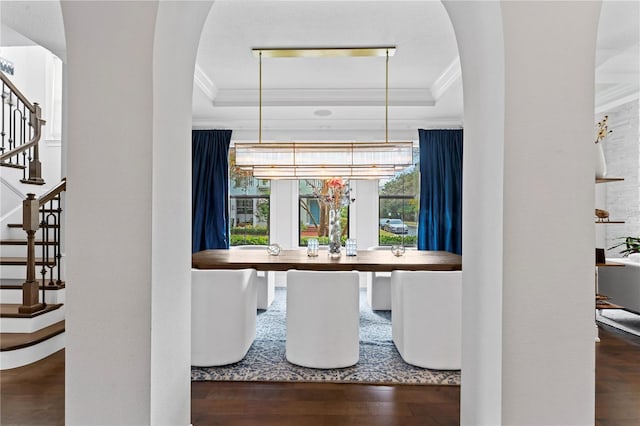 dining room featuring arched walkways, a raised ceiling, ornamental molding, wood finished floors, and stairs