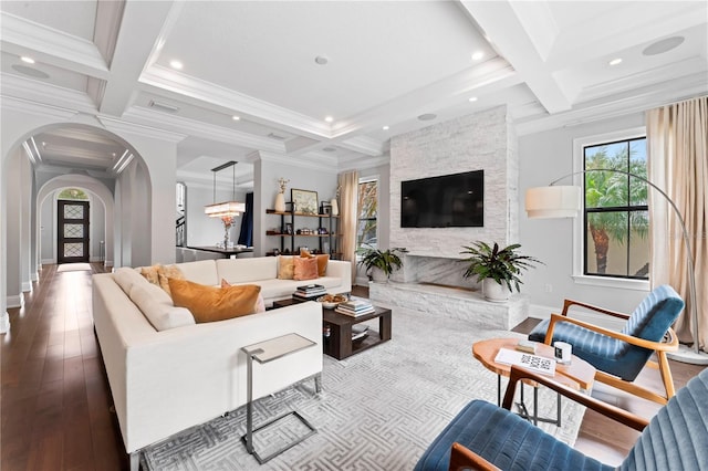 living area with arched walkways, beam ceiling, wood finished floors, coffered ceiling, and baseboards