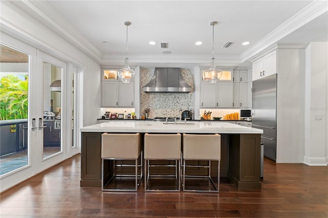 kitchen featuring visible vents, light countertops, ornamental molding, wall chimney range hood, and stainless steel built in fridge